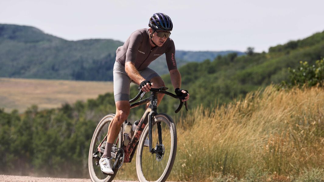Gravel cyclist riding with mounted accessories on a dusty trail, showcasing gear for off-road adventures