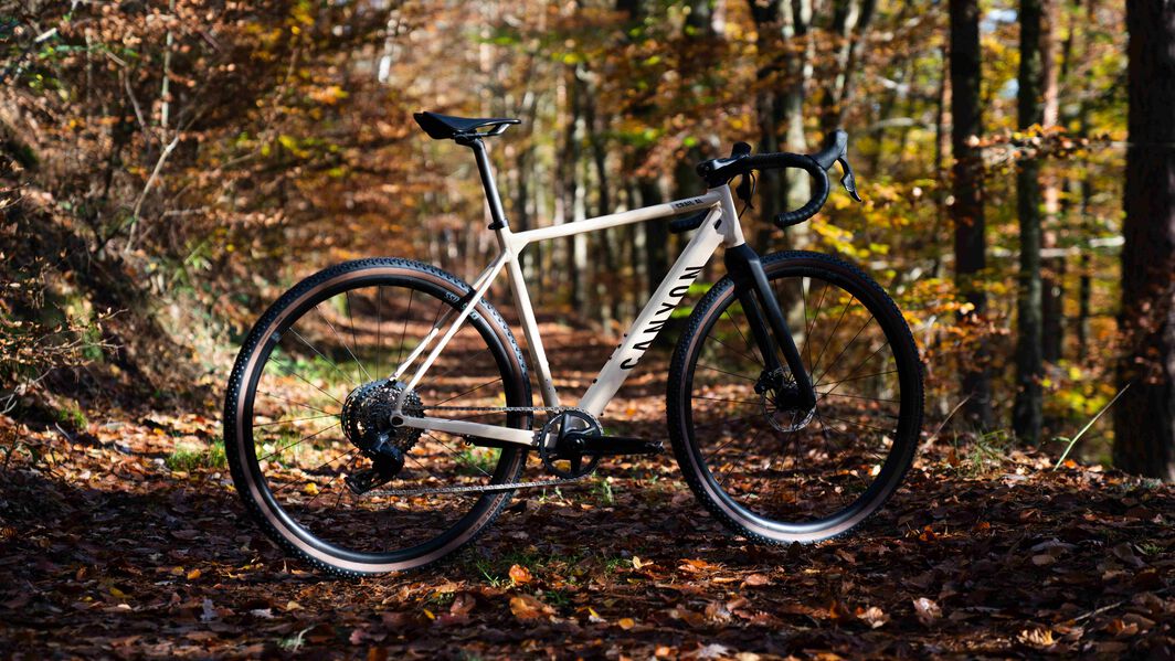 Canyon Grail CF gravel bike with wide tire clearance, built for rugged trails and shown in a forest. Canyon gravel bike with wide tire clearance for rugged trails, shown in a serene forest setting during fall