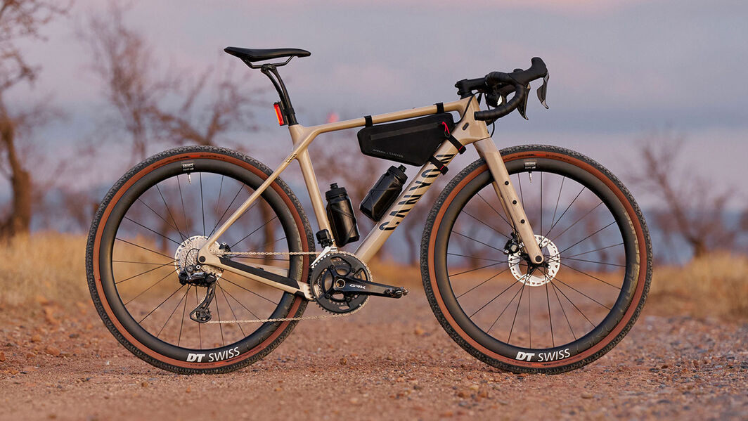 Canyon Grizl grussykkel – eventyrklar oppsett med bikepacking-utstyr Canyon Grizl grussykkel med oppsett for bikepacking, inkludert rammeveske og doble vannflasker, vist på en støvete sti med DT Swiss-hjul.